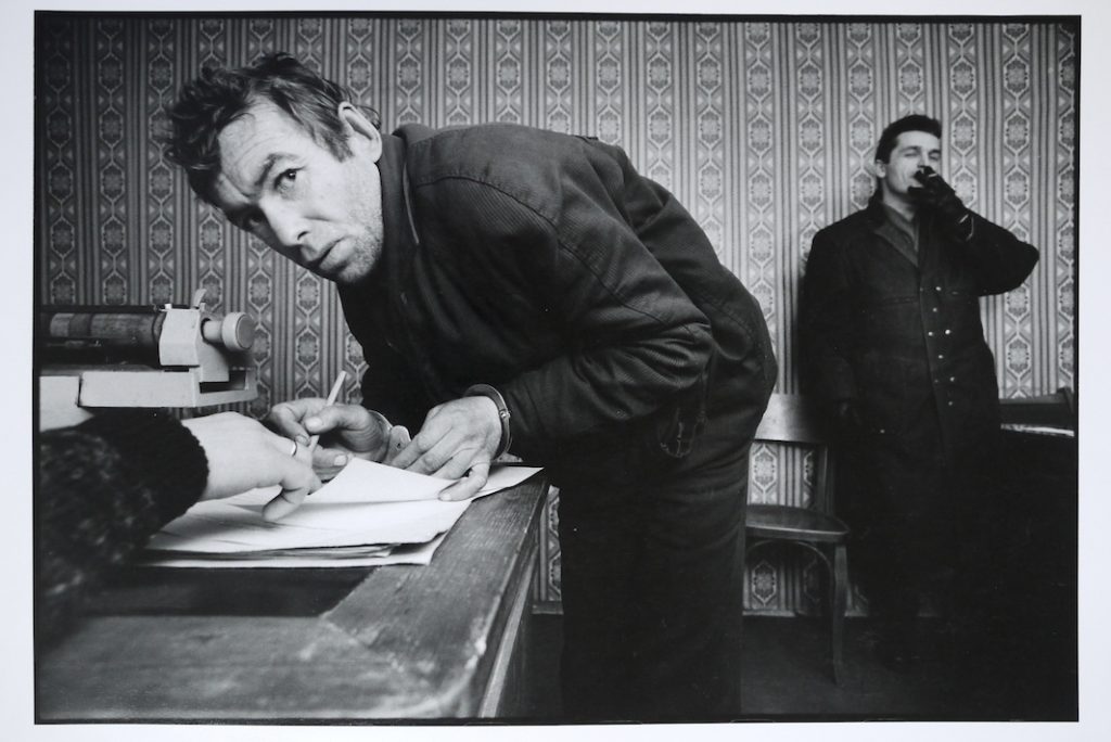 A petty thief signing his confesion at the local police station.  the arresting officer stands in the background.