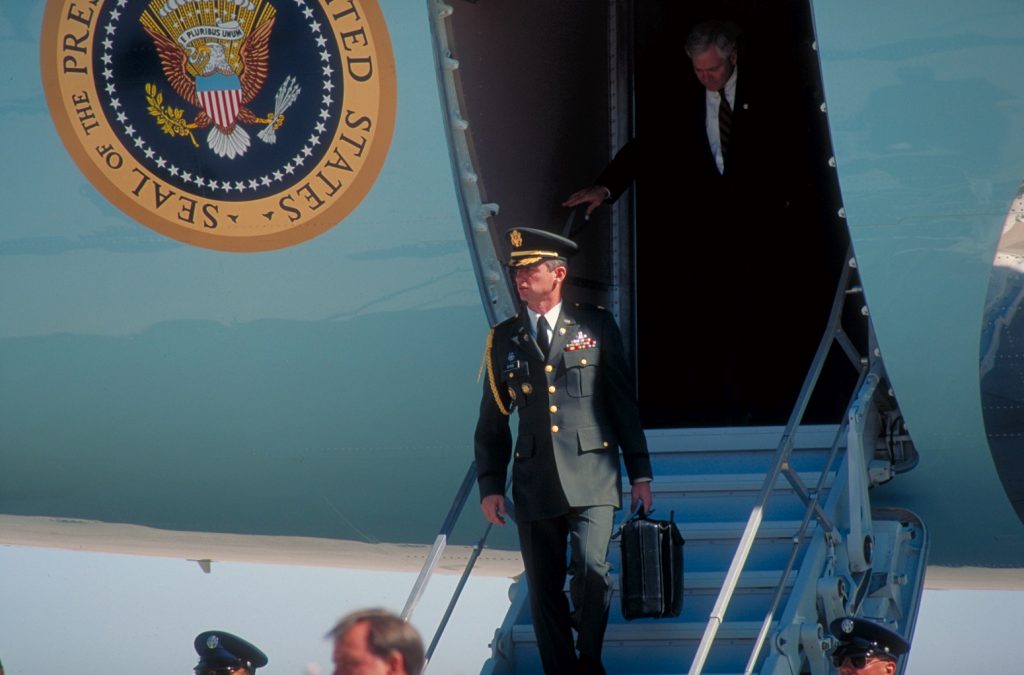 Dep. NSC Adviser Bob Gates de- planing, w. football carrier (mil. aide w. briefcase-carried nuclear missile launch code), in fore, (w. campaigning Pres. Bush) in CA.  (Photo by Diana Walker//Time Life Pictures/Getty Images)