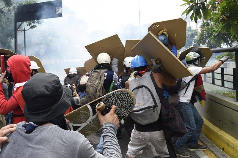 Opposition activists use makeshift shields to cover themselves, as clashes with police erupt during a protest against President Nicolas Maduro, in Caracas on May 8, 2017.Venezuela's opposition mobilized Monday in fresh street protests against President Nicolas Maduro's efforts to reform the constitution in a deadly political crisis. Supporters of the opposition Democratic Unity Roundtable (MUD) gathered in eastern Caracas to march to the education ministry under the slogan "No to the dictatorship." / AFP PHOTO / JUAN BARRETO