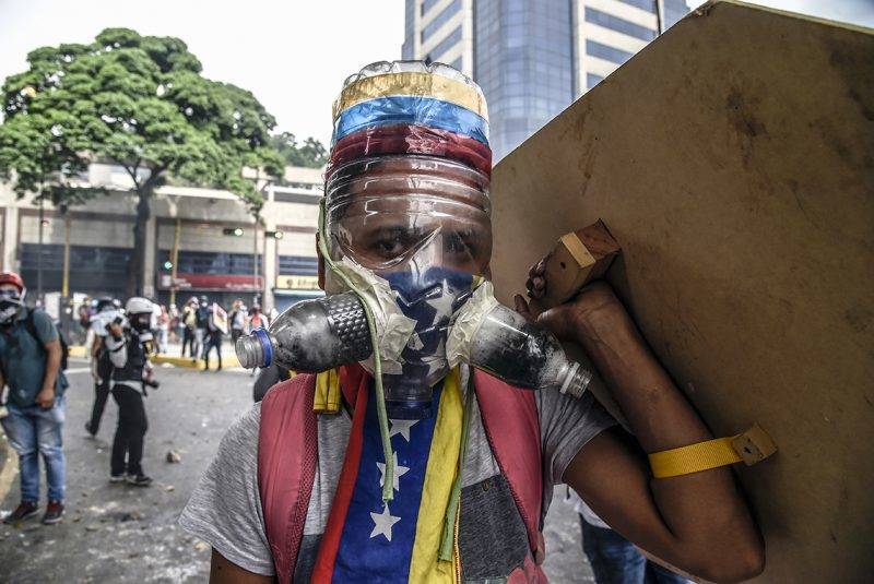 A Venezuelan opposition activist wearing a homemade gas mask takes cover behind a makeshift shield as clashes erupt with riot police during a protest against President Nicolas Maduro, in Caracas on May 8, 2017.Venezuela's opposition mobilized Monday in fresh street protests against President Nicolas Maduro's efforts to reform the constitution in a deadly political crisis. Supporters of the opposition Democratic Unity Roundtable (MUD) gathered in eastern Caracas to march to the education ministry under the slogan "No to the dictatorship." / AFP PHOTO / JUAN BARRETO