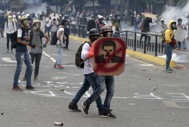 Venezuelan opposition activists take cover  behind a makeshift shield in clashes with the riot police during a protest against President Nicolas Maduro, in Caracas on May 8, 2017.Venezuela's opposition mobilized Monday in fresh street protests against President Nicolas Maduro's efforts to reform the constitution in a deadly political crisis. Supporters of the opposition Democratic Unity Roundtable (MUD) gathered in eastern Caracas to march to the education ministry under the slogan "No to the dictatorship." / AFP PHOTO / JUAN BARRETO