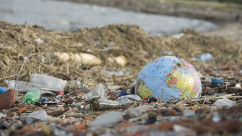 Globe partially buried in rubble and garbage littering beach