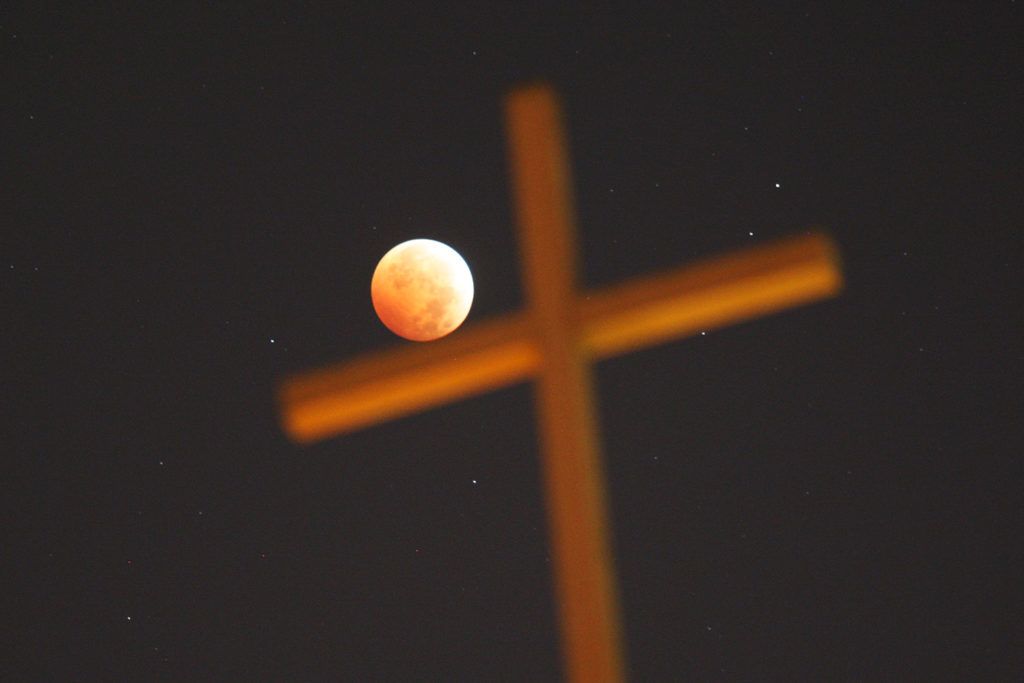 LOS ANGELES, CA - OCTOBER 8: A religious cross is seen as the moon is illuminated by sunlight reflected off the Earth during a total lunar eclipse, one of four so-called "blood moons", on October 8, 2014 in Los Angeles, California. The first in the current tetrad of blood moons fell on Passover and the current eclipse occurs on the Jewish holiday of Sukkot, the fifth day after Yom Kippur, leading some religious people to believe that it is a prophetic sign of the end times of civilization. This blood moon appears 5.3% larger than the last one on April 15 because it occurs right after the perigee, the closest point in its orbit to the Earth.   David McNew/Getty Images/AFP