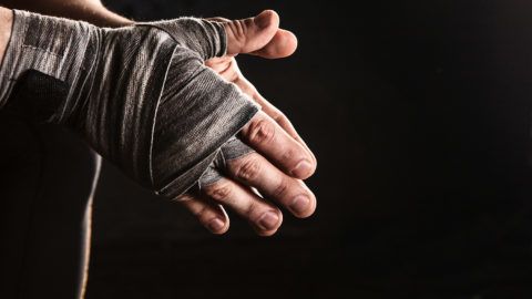 Close-up hand with bandage of muscular man training kickboxing  on black