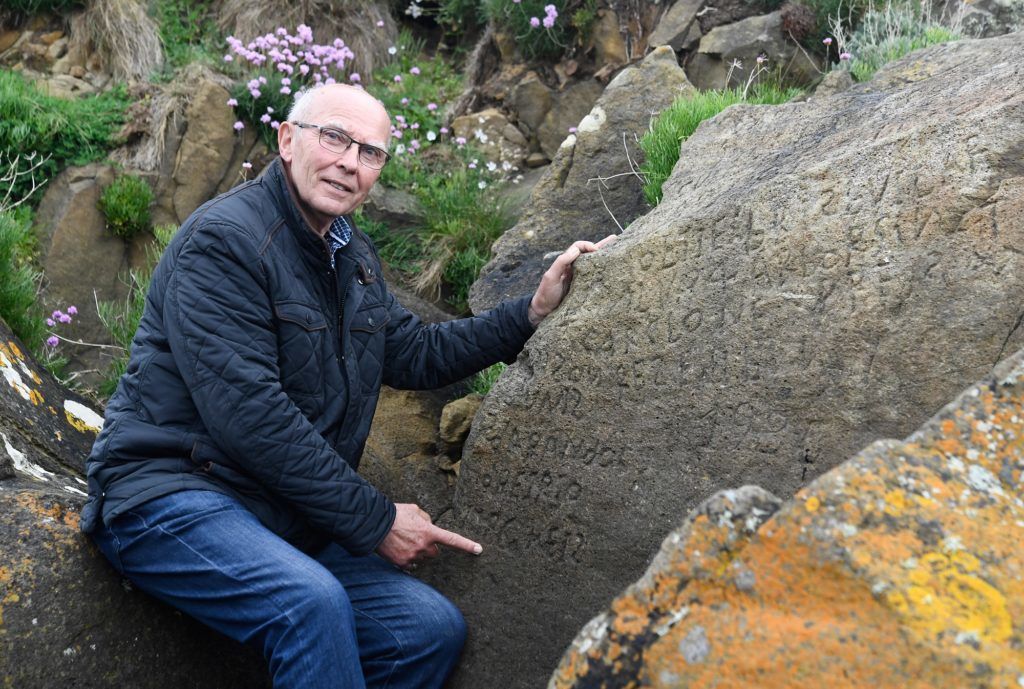 French local councillor in charge of small heritage Michel Paugam poses on May 7, 2019 as he shows inscriptions composing indecipherable words on a rock in the Brittany village of Plougastel-Daoulas. - The city launched a national call with a 2000 euros reward to anyone able to solve the mystery of those inscriptions propably made during the 18th century. (Photo by Fred TANNEAU / AFP)
