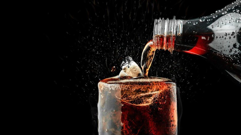 Pour soft drink in glass with ice splash on dark background.